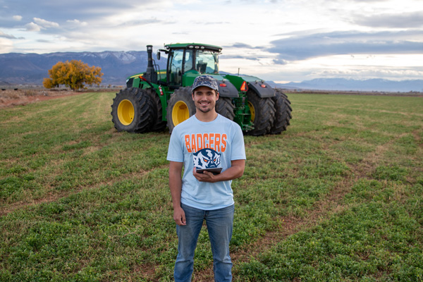 Snow College student standing in front of a tractor holding an iPad.