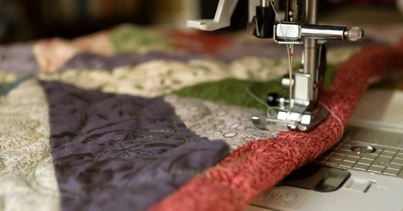Sewing machine sewing a multi-color quilt edge.
